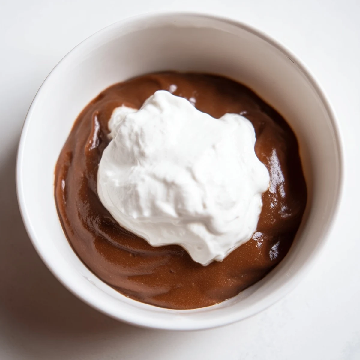 Silky chocolate pudding with cream in glass serving dishes, topped with a rich dollop.
