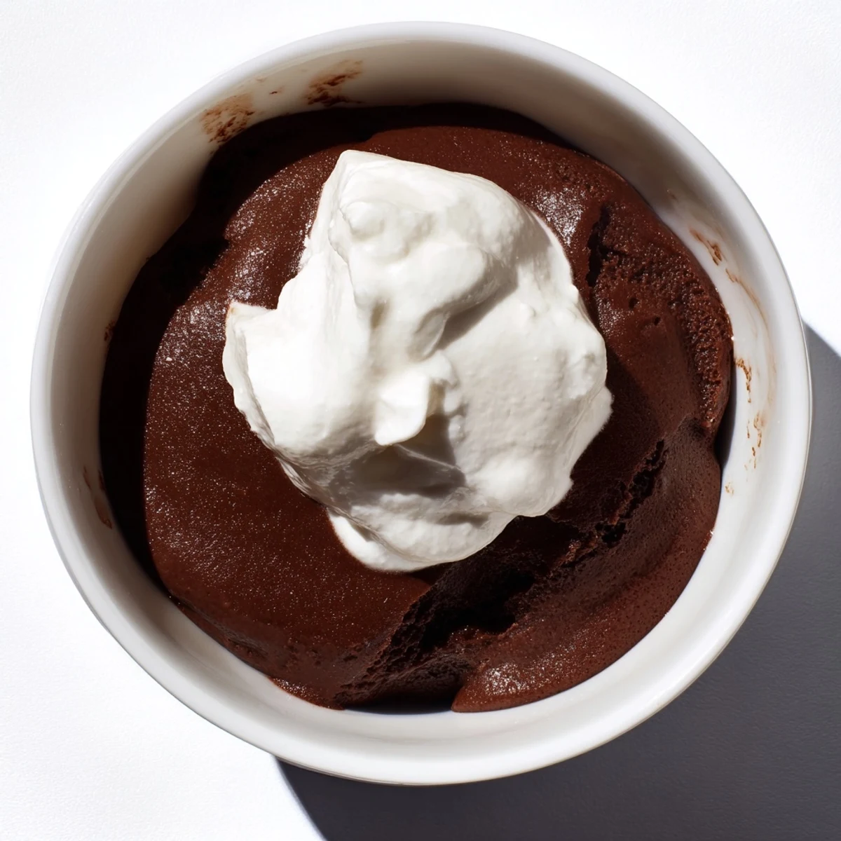 Rich chocolate pudding with cream layered in jars, garnished with a swirl of fresh toppings.