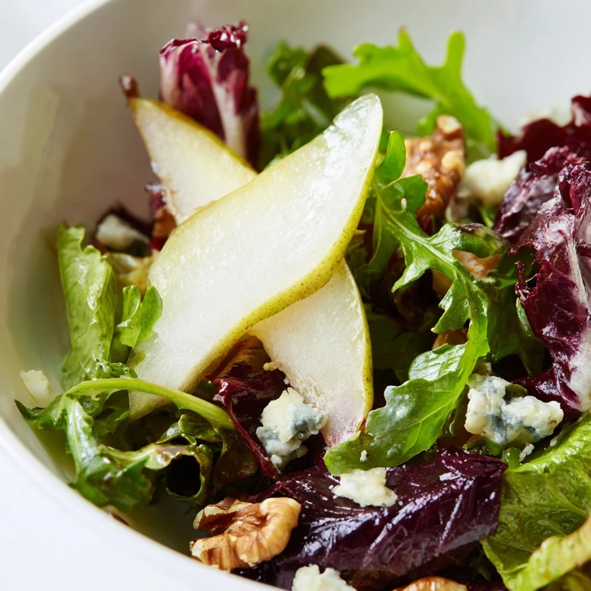 Winter Green Salad with Pears served on a white platter, showcasing crisp greens, juicy pear slices, and toasted walnuts.