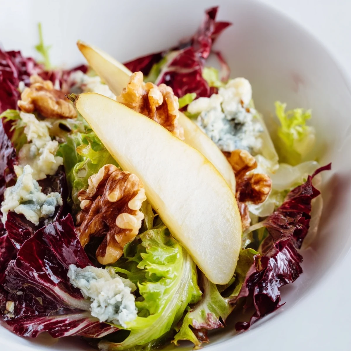A close-up of Winter Green Salad with Pears featuring tangy blue cheese crumbles and a glistening apple cider vinaigrette.
