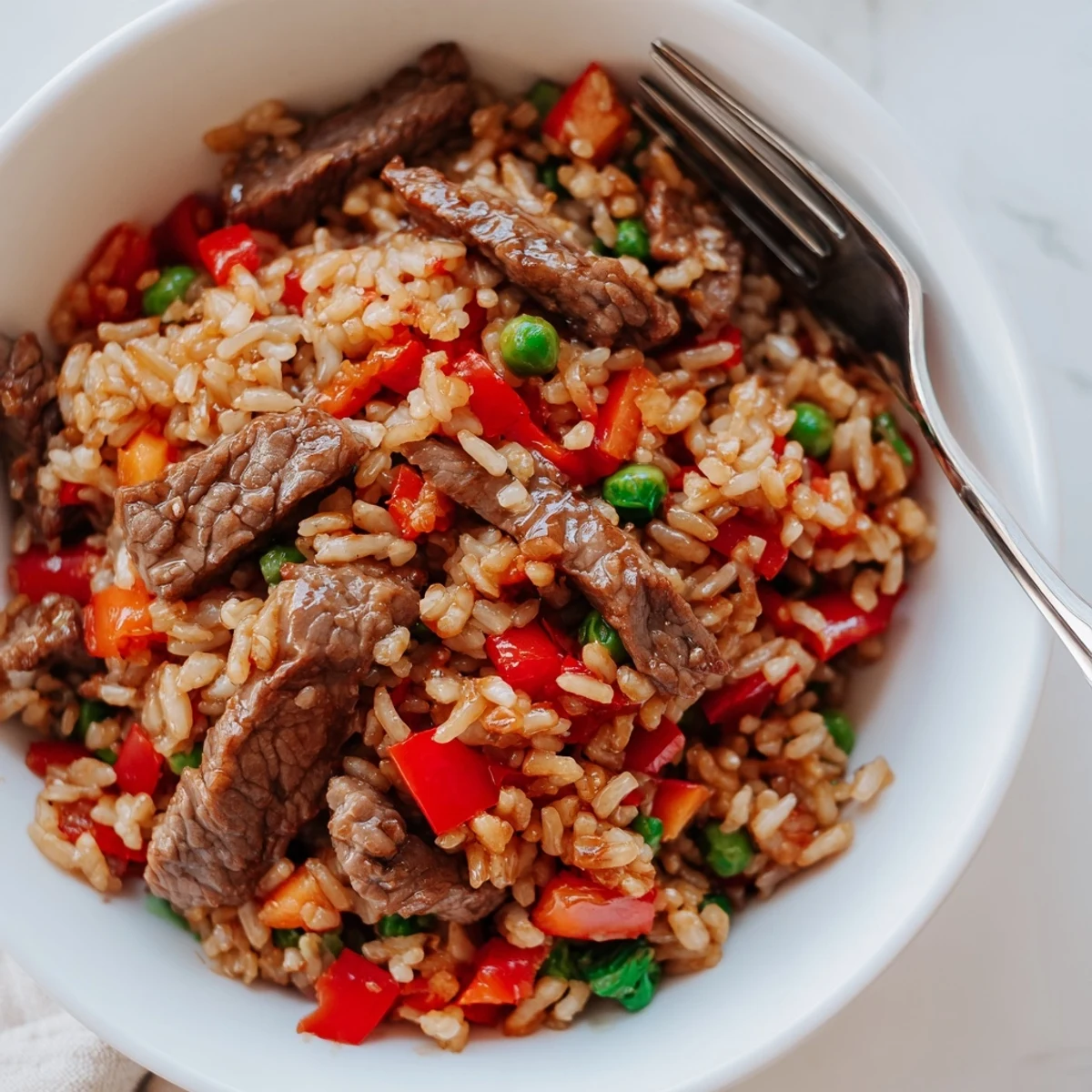Beef Fried Rice with Vegetables is served hot and steaming with colorful diced carrots, red bell peppers, and green peas.