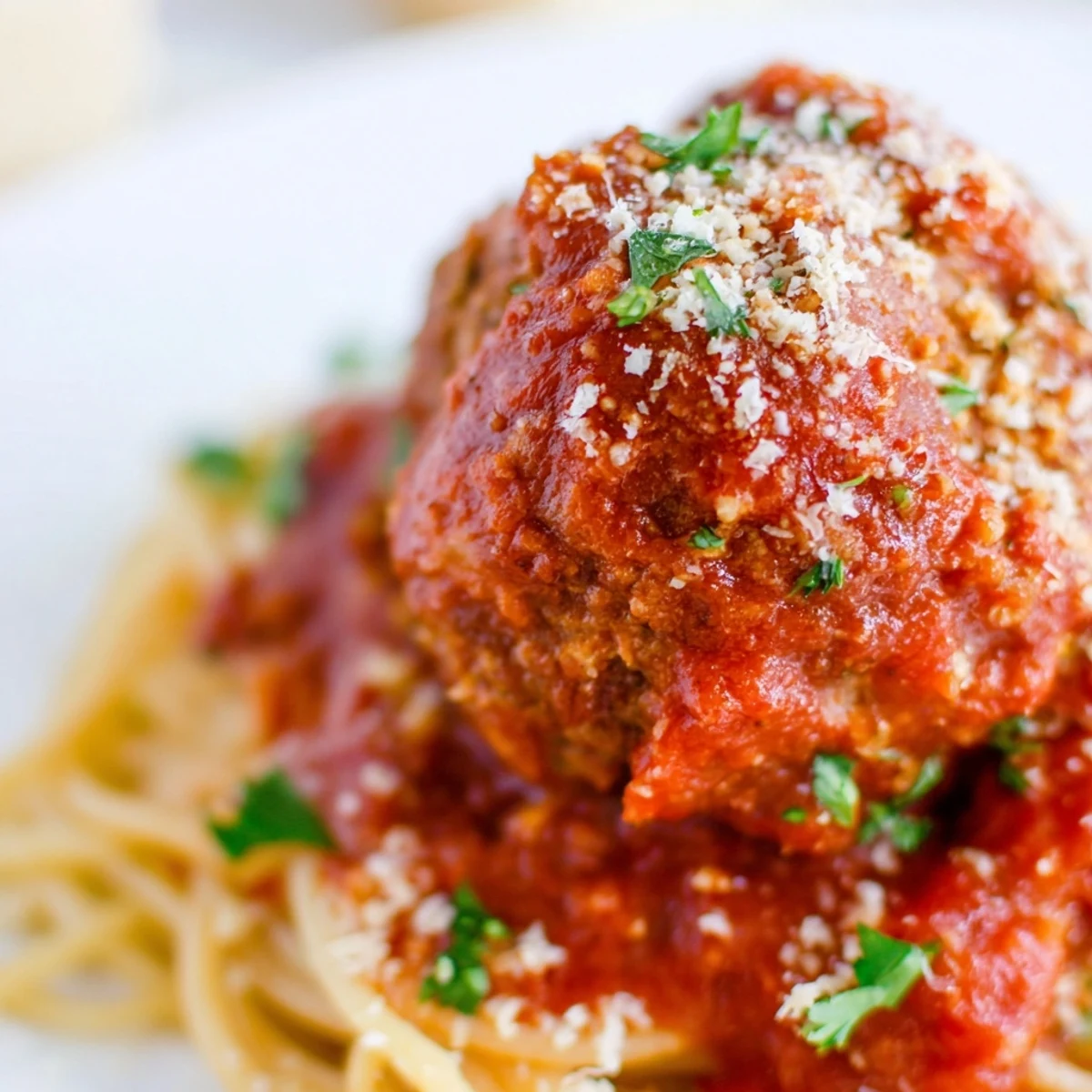 Perfectly browned Turkey Meatballs with Marinara Sauce and Spaghetti sit in a white bowl garnished with fresh basil.