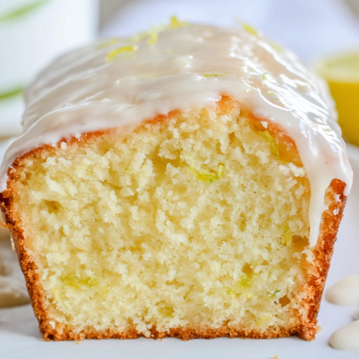 Slice of moist Lemon Loaf Cake revealing a soft interior and bright lemon zest, served on a rustic plate with fresh berries.