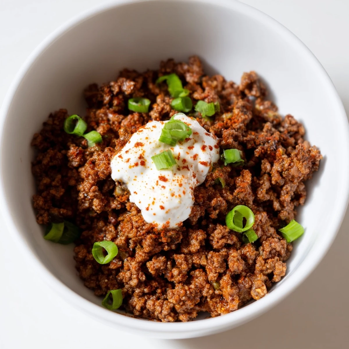 Topped with shredded cheese and sour cream, this Beef Burrito Bowl is garnished with fresh cilantro and lime wedges.