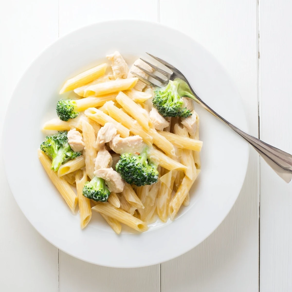 A close-up view of Creamy Broccoli Pasta with Chicken in a white bowl, garnished with fresh parsley and extra Parmesan, steam rising from the rich sauce.  