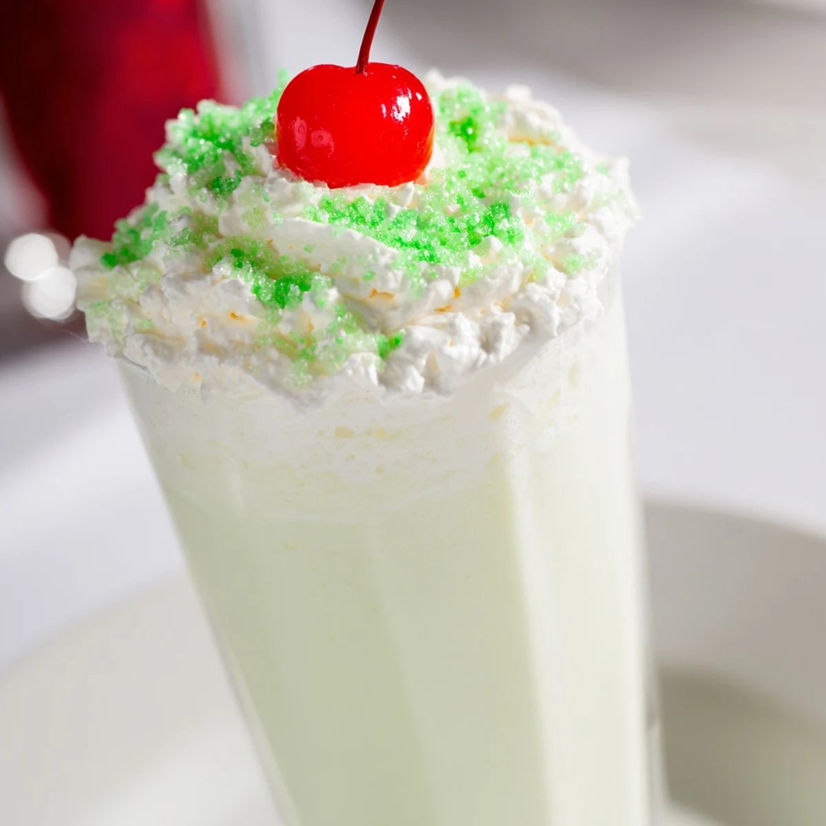 Festive Shamrock Shake with Whipped Cream served in a chilled glass, garnished with green sanding sugar, ready to drink with a straw.