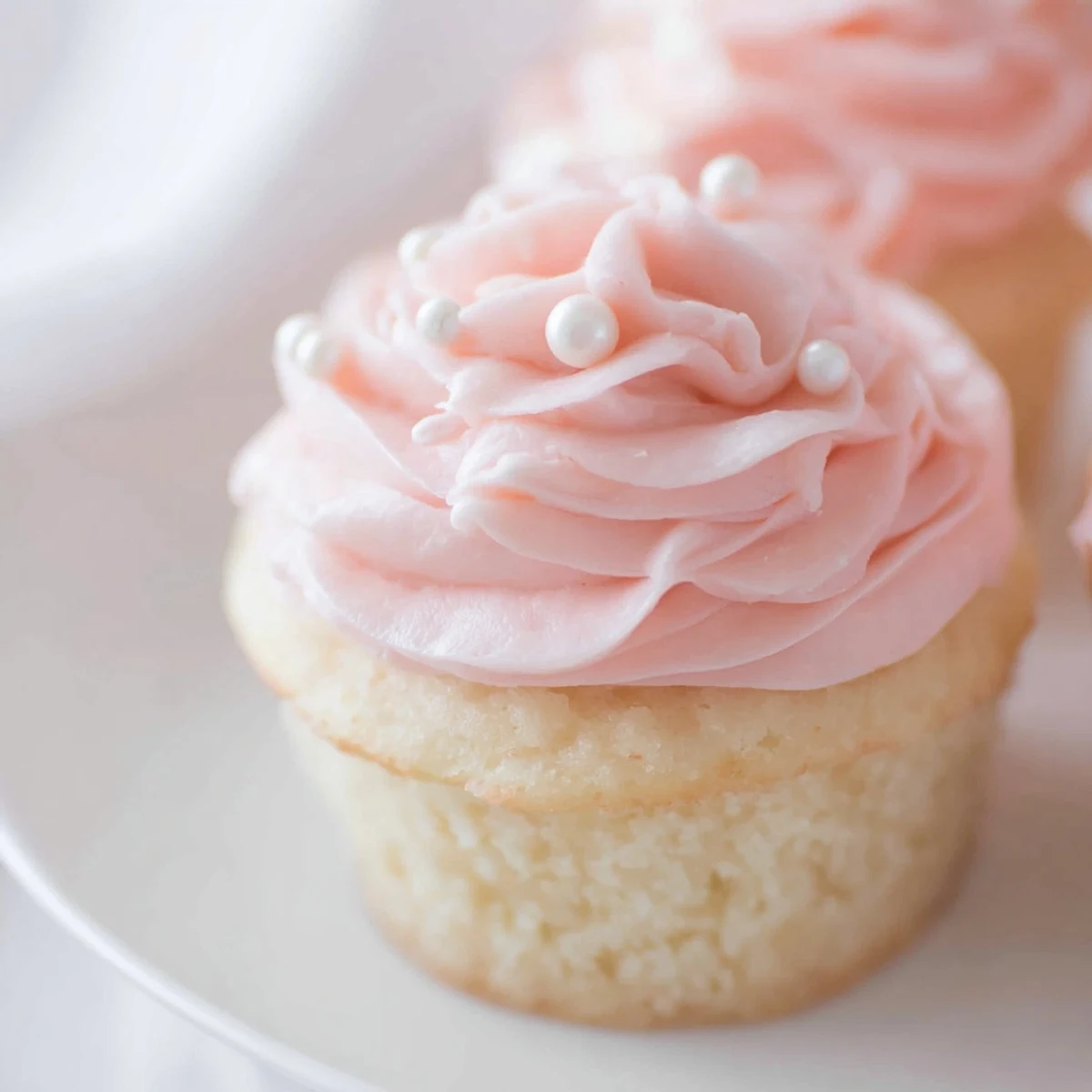 Tender Pink Champagne Cupcakes with fluffy buttercream swirls and festive sprinkles, displayed on a cooling rack with a bowl of pink champagne nearby.
