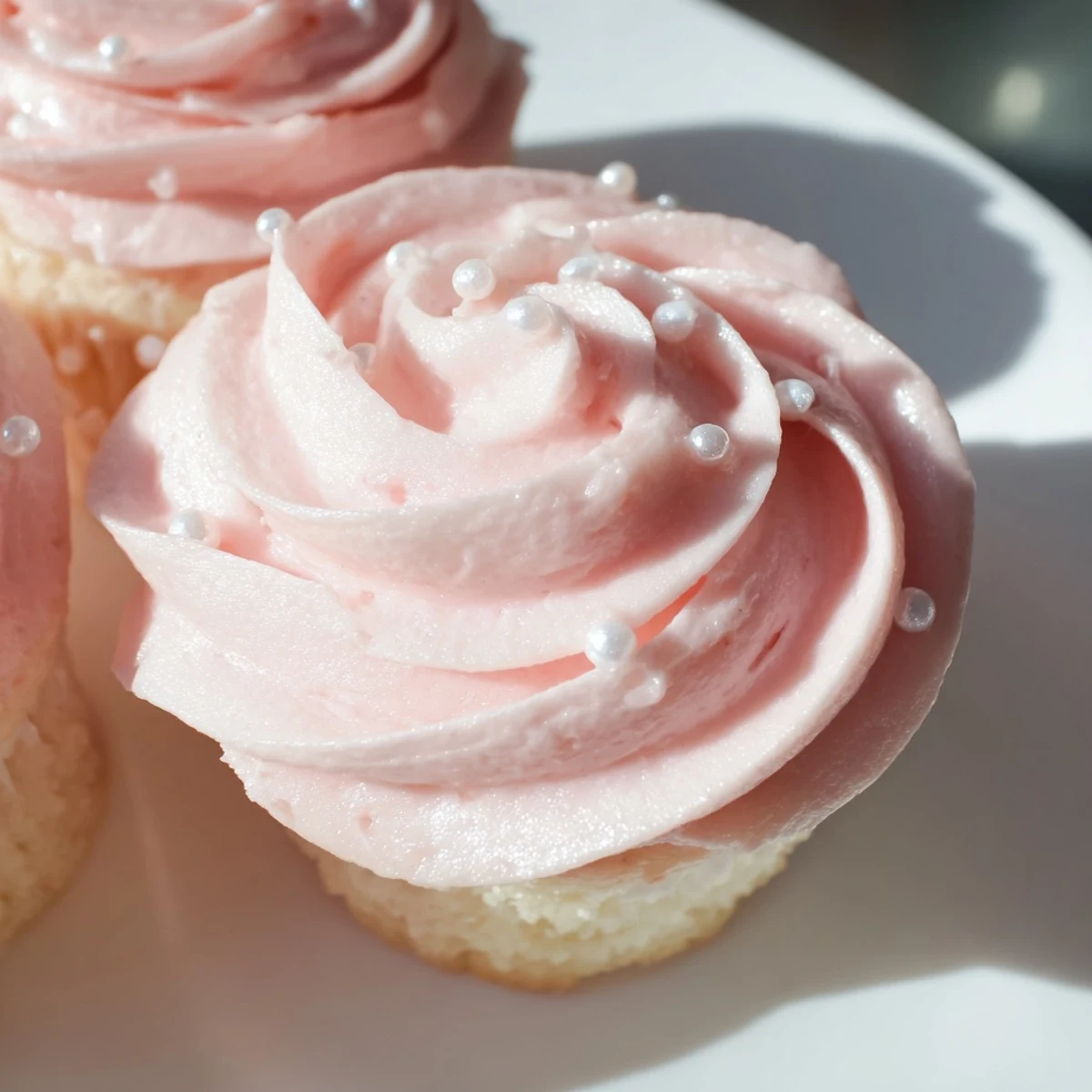 Delicate Pink Champagne Cupcakes with a moist crumb and pale pink frosting, served individually on small dessert plates ready for a birthday party.