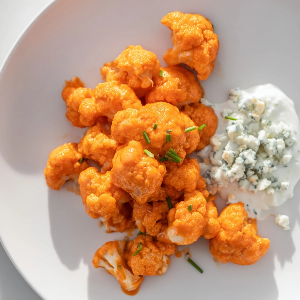 Golden, crispy buffalo cauliflower wings with blue cheese dip and fresh celery sticks on a rustic serving platter.