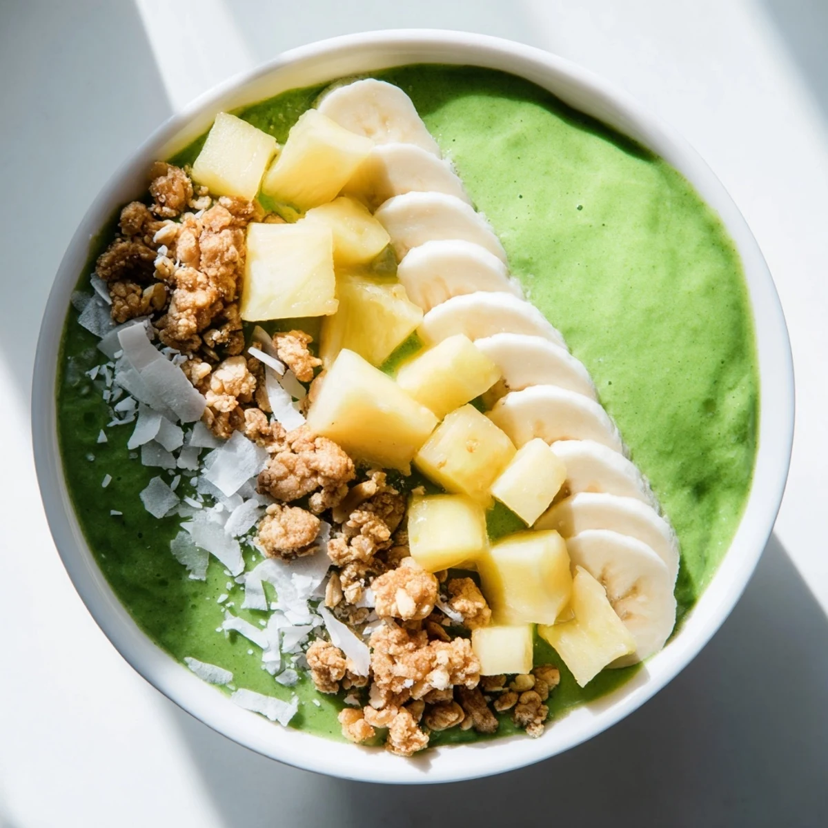 Colorful vegan green smoothie bowl featuring creamy spinach and pineapple base, topped with berries and almond butter for extra flavor.