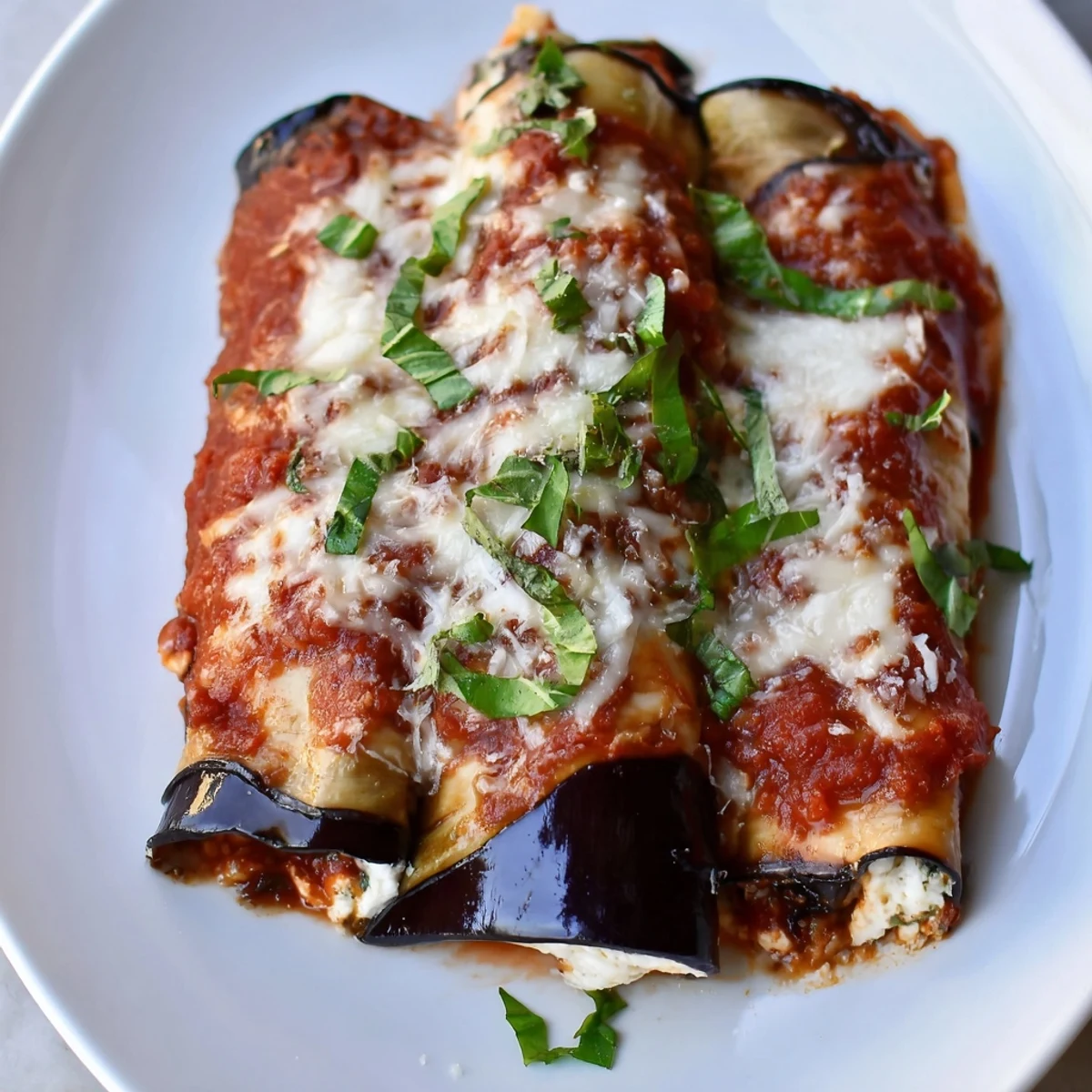 Savory Baked Eggplant Rollatini with Ricotta Cheese features tender eggplant wrapped around herby ricotta, smothered in rich tomato sauce and bubbly golden mozzarella cheese.