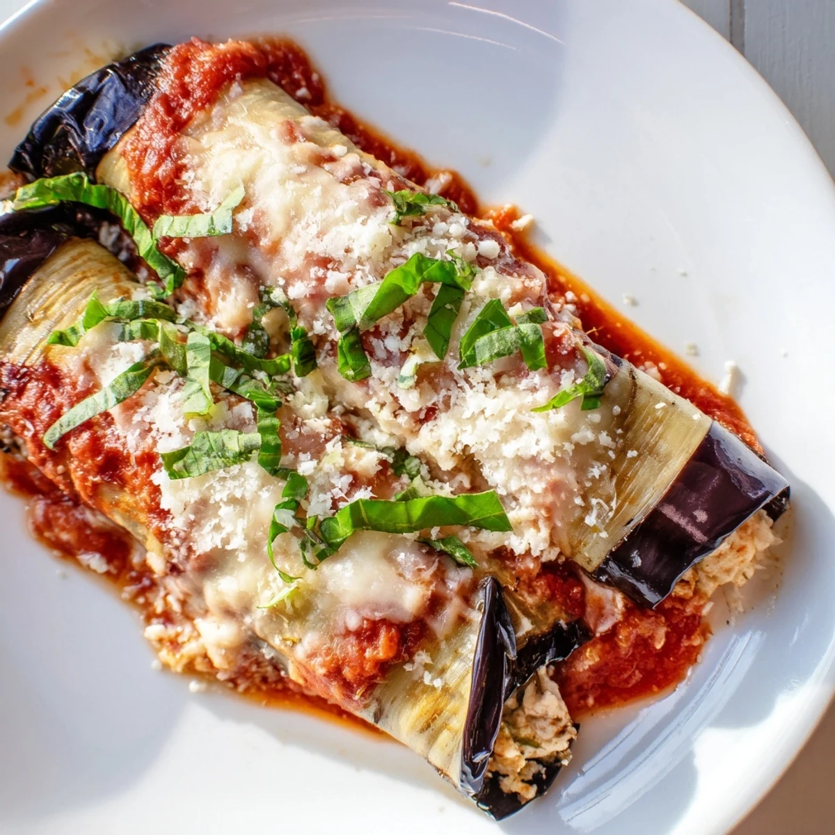 A close-up of Baked Eggplant Rollatini with Ricotta Cheese shows rolled eggplant stuffed with creamy ricotta, baked until golden and served on a rustic dinner plate.