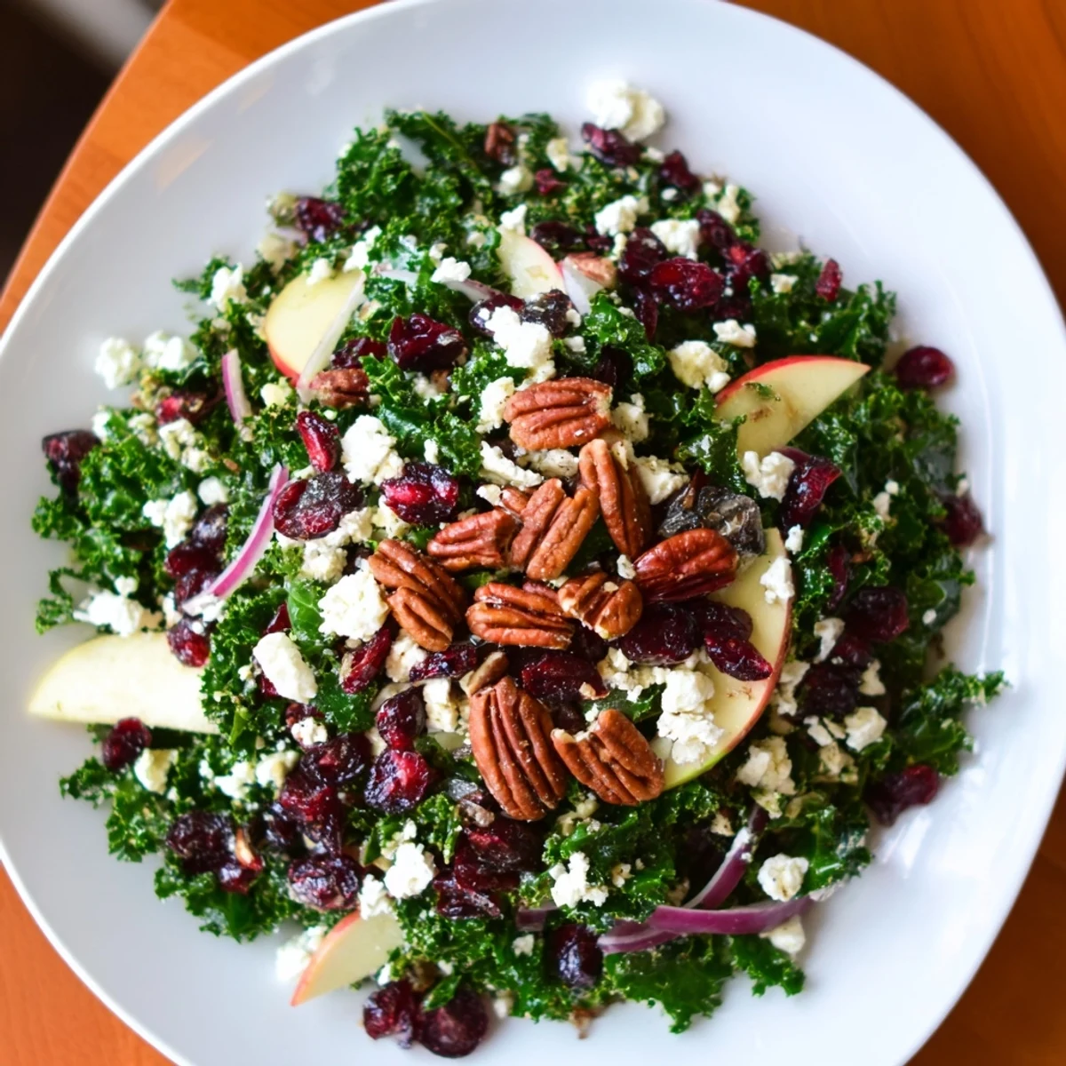 A close-up of Winter Kale Salad with Pecans and Cranberries shows crisp kale, sliced apple, and crumbled feta on a rustic wooden serving board.