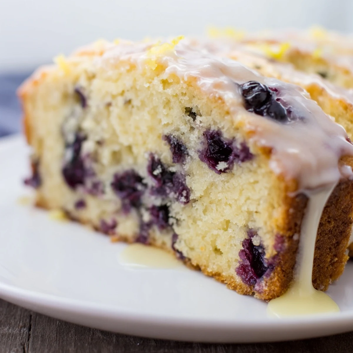 Freshly baked Lemon Blueberry Yogurt Loaf Cake on parchment, sliced with glaze dripping for serving.