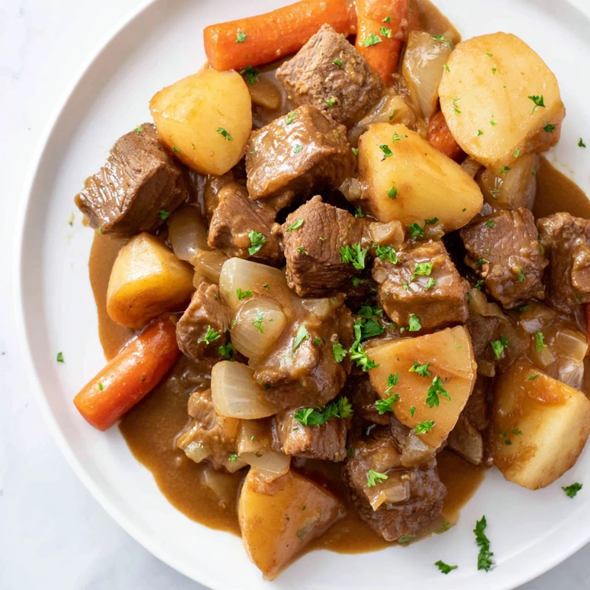 A bowl of Irish Beef Stew with Rich Brown Gravy features tender beef chunks, soft carrots, and potatoes in a glossy, dark sauce.