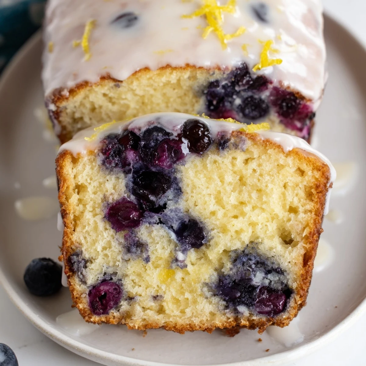 A close-up of Lemon Blueberry Yogurt Loaf Cake with Glaze, glistening and moist with scattered fresh blueberries.