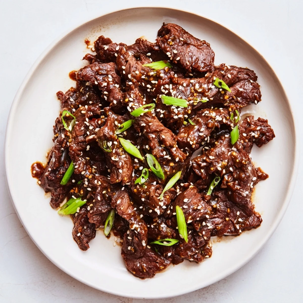 A close-up of Slow Cooker Korean Beef shredded and glistening with savory-sweet sauce, garnished with fresh green onions and sesame seeds.