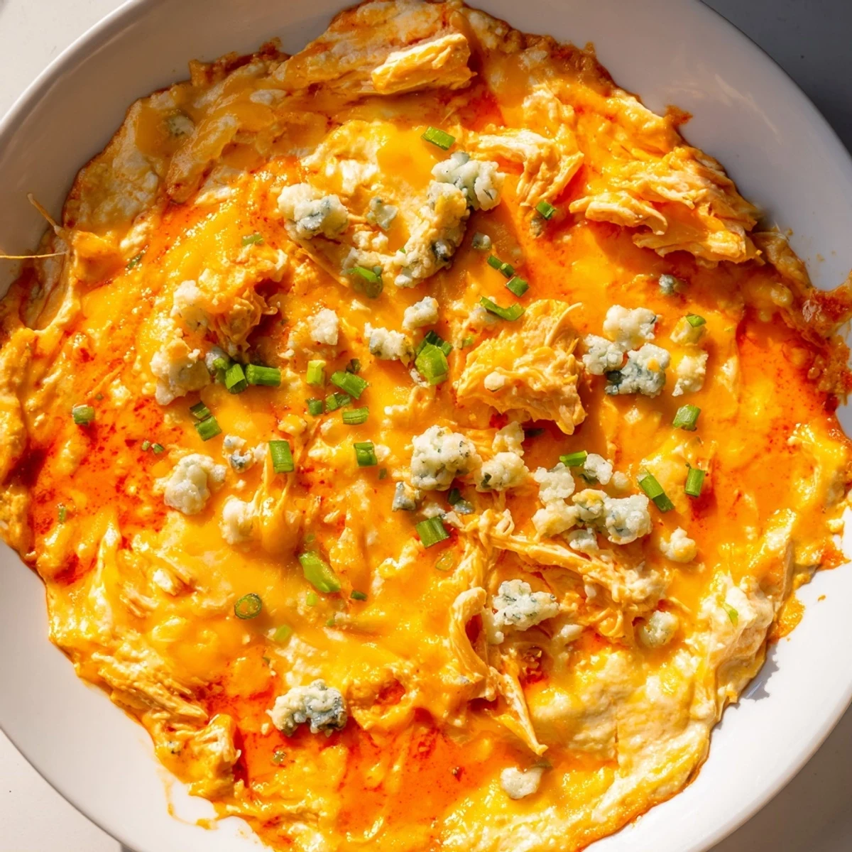 Creamy Keto Buffalo Chicken Dip bubbling in a baking dish, topped with melted cheese and fresh green onions, served with celery sticks.