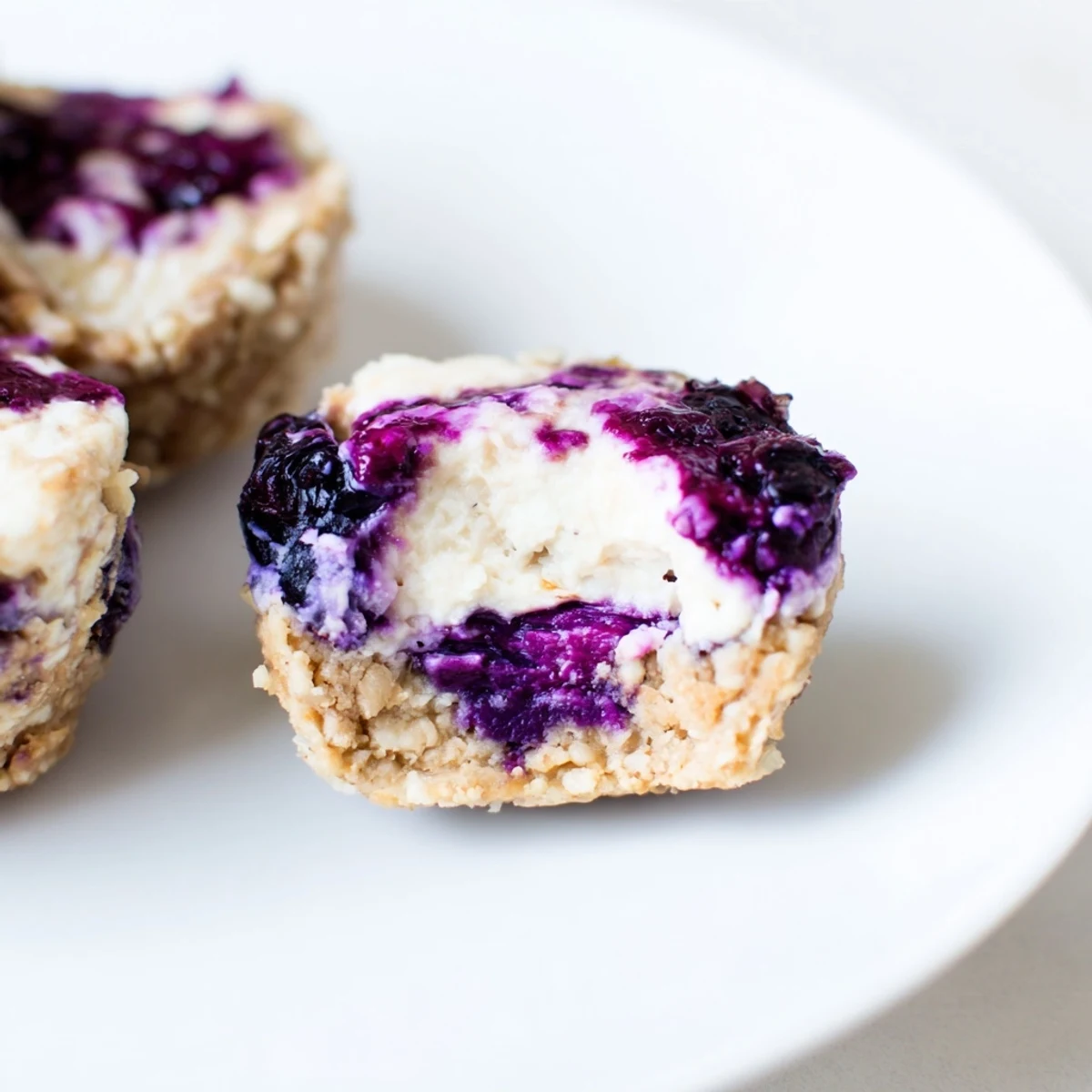 A close-up of Blueberry Cheesecake Protein Bites on a wooden board, graham cracker crumbs sprinkled around. 