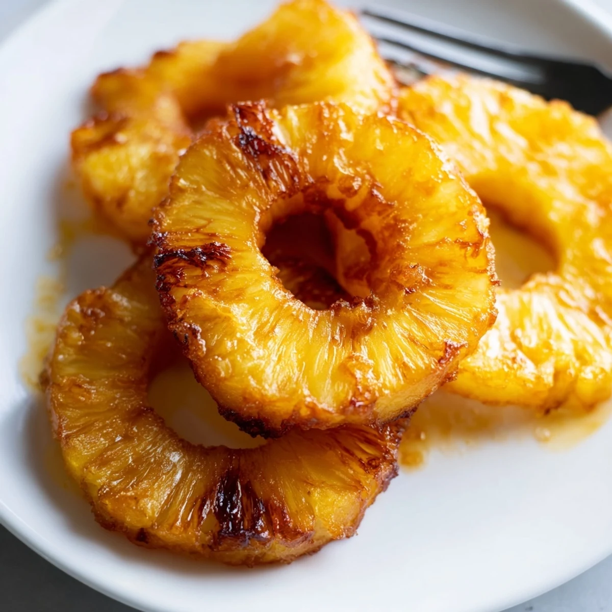 Golden rum-soaked fried pineapple slices glisten on a plate, served warm with a scoop of vanilla ice cream melting beside them.