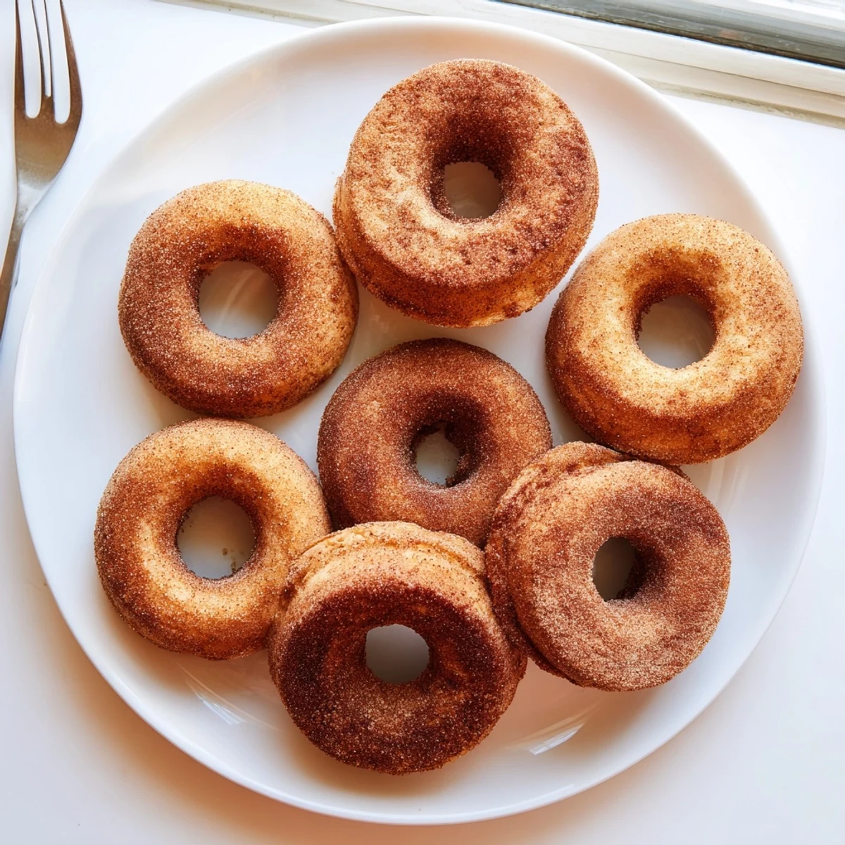 Golden-brown Delicious Baked Cinnamon Sugar Donuts rest on a cooling rack, their sugary coating sparkling.