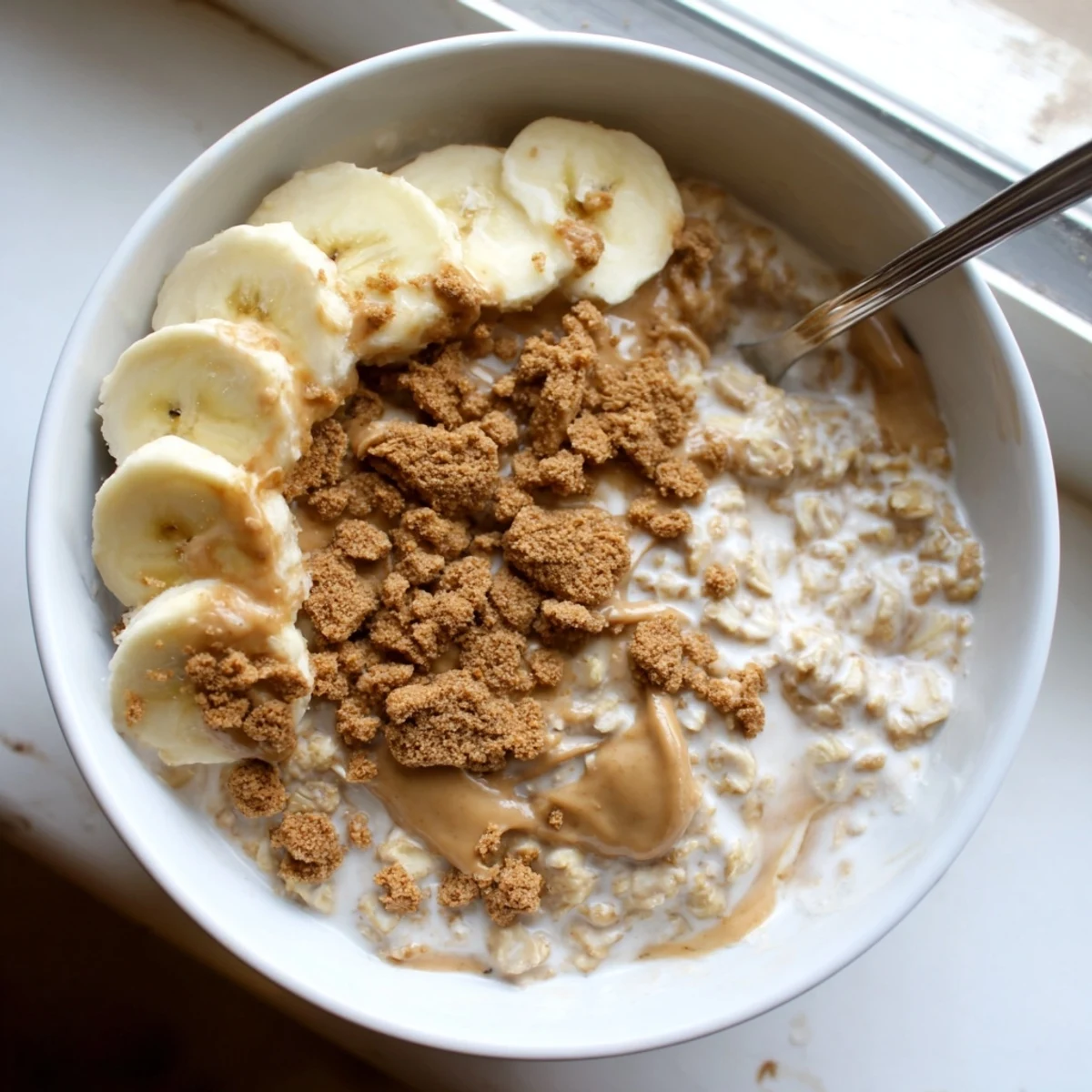 The finished Quick Biscoff Overnight Oats in a glass jar, topped with crushed cookies and fresh banana slices for a sweet breakfast.