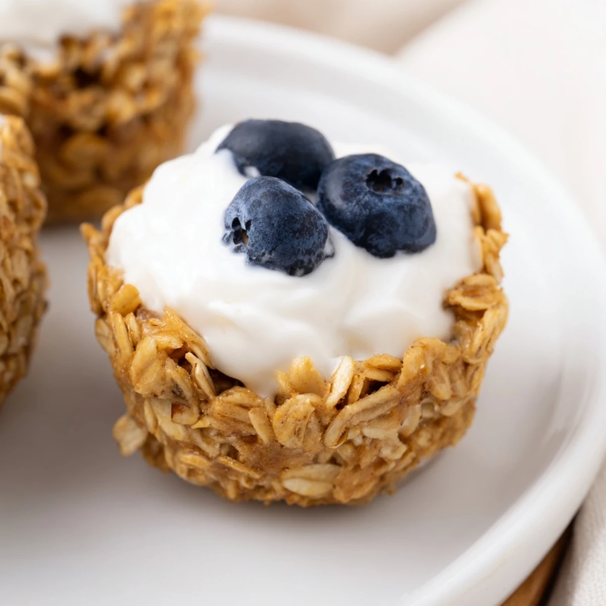 Soft-baked oatmeal cups with creamy Greek yogurt and blueberries, served on a rustic wooden board for an easy grab-and-go snack.