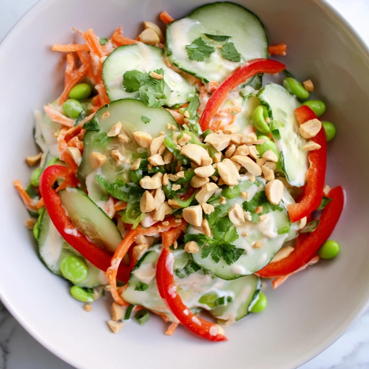 A close-up of the Creamy Asian Cucumber Bowl with glistening sliced cucumbers, crisp carrots, and red bell peppers tossed in a creamy dressing.