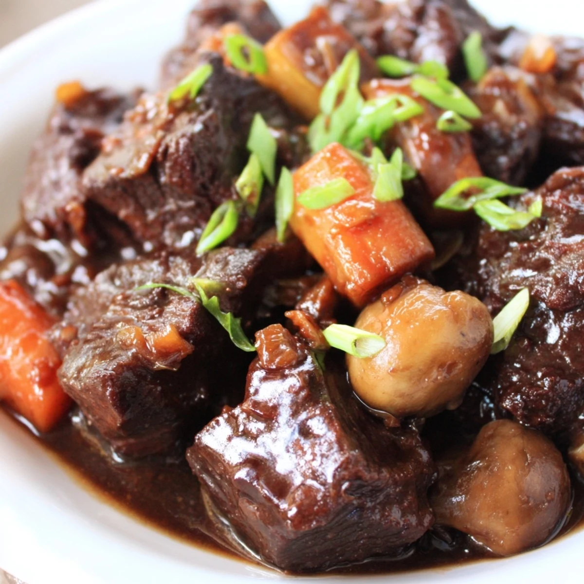 Fork-tender Asian Style Slow Cooked Beef Cheeks With Mushrooms plated over creamy mashed potatoes, garnished with fresh cilantro and sliced green onions for a vibrant touch.