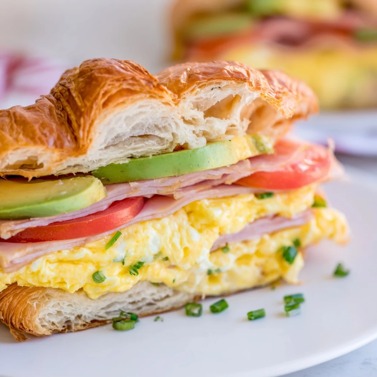 Freshly baked croissant breakfast sandwich filled with fluffy eggs, melted cheese, and avocado slices.