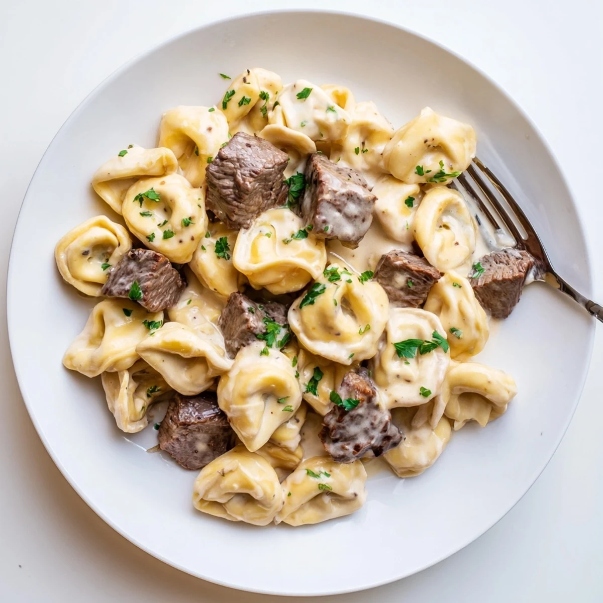 Close-up of Garlic Steak Tortellini with seared steak bites and cheese tortellini in a glossy garlic cream sauce, garnished with fresh parsley.