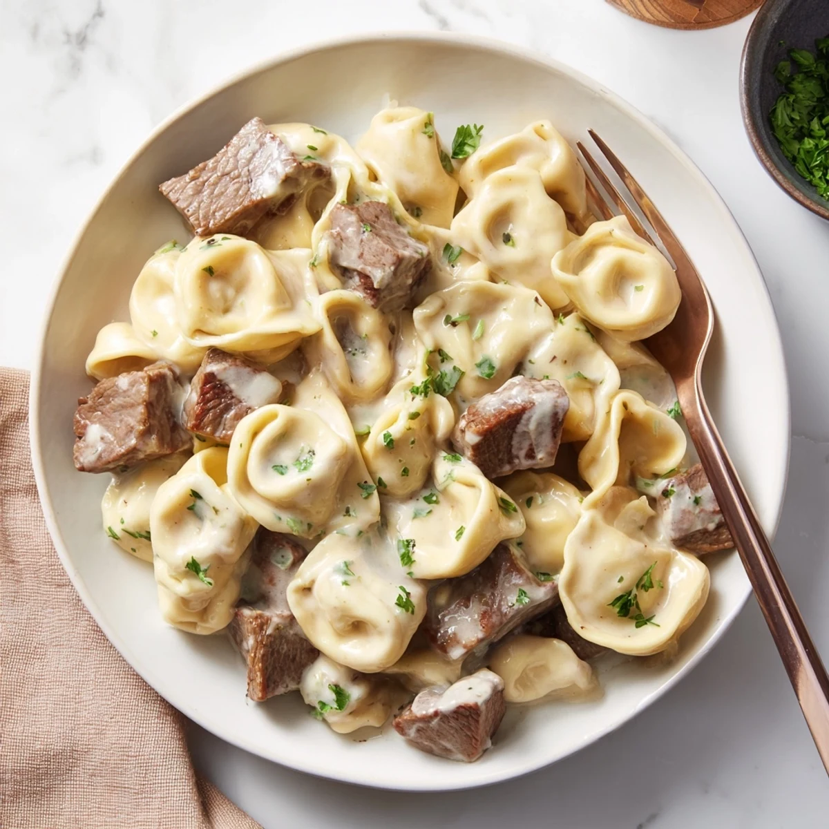 A skillet of Garlic Steak Tortellini next to a glass of red wine, showing a rich sauce coating pasta and tender beef pieces.