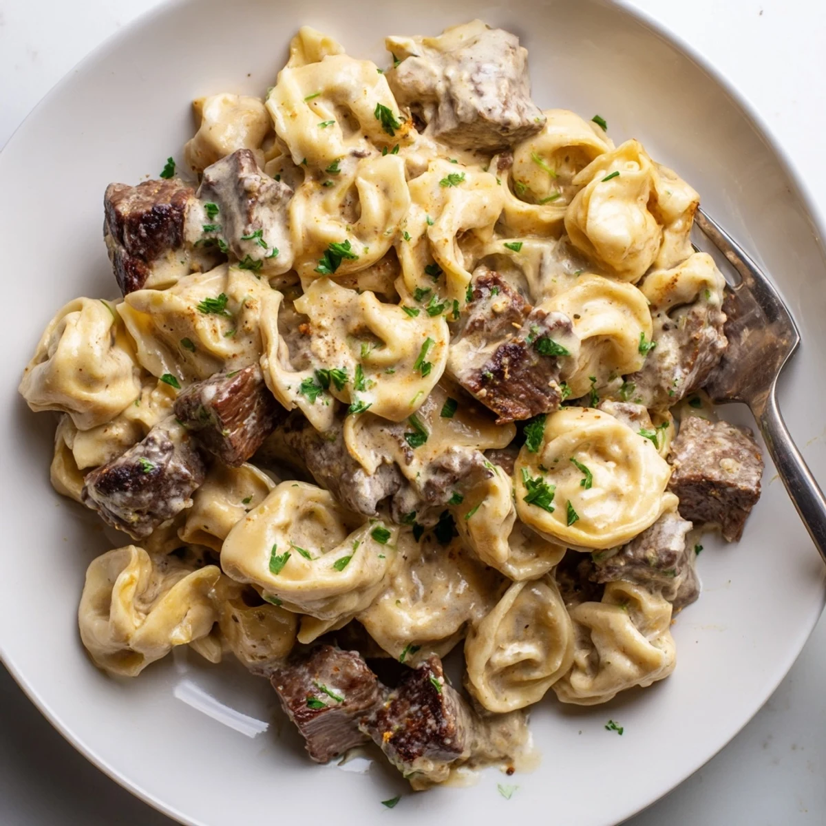 Garlic Steak Tortellini plated in a shallow bowl with extra Parmesan, steam rising from the warm Italian-American main dish.