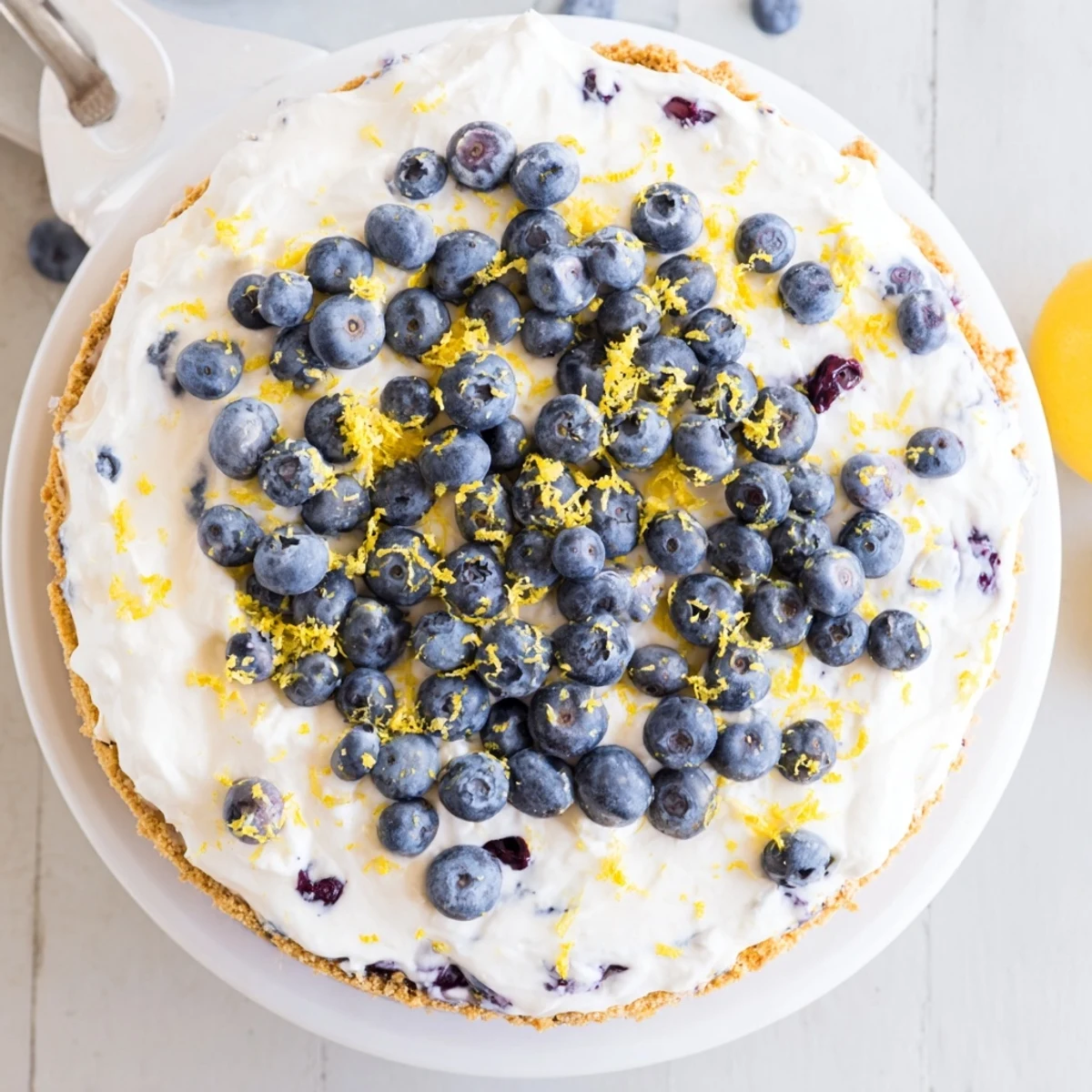 No bake lemon blueberry cream cake topped with fresh berries and lemon zest on a graham cracker crust