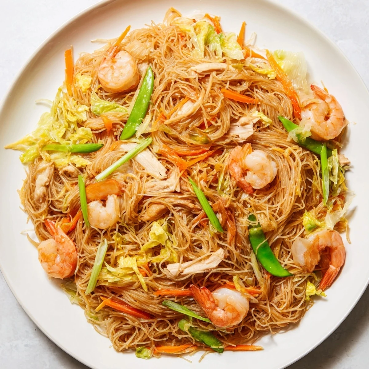 Steaming plate of savory Pancit Bihon stir-fry with colorful vegetables and rice vermicelli noodles