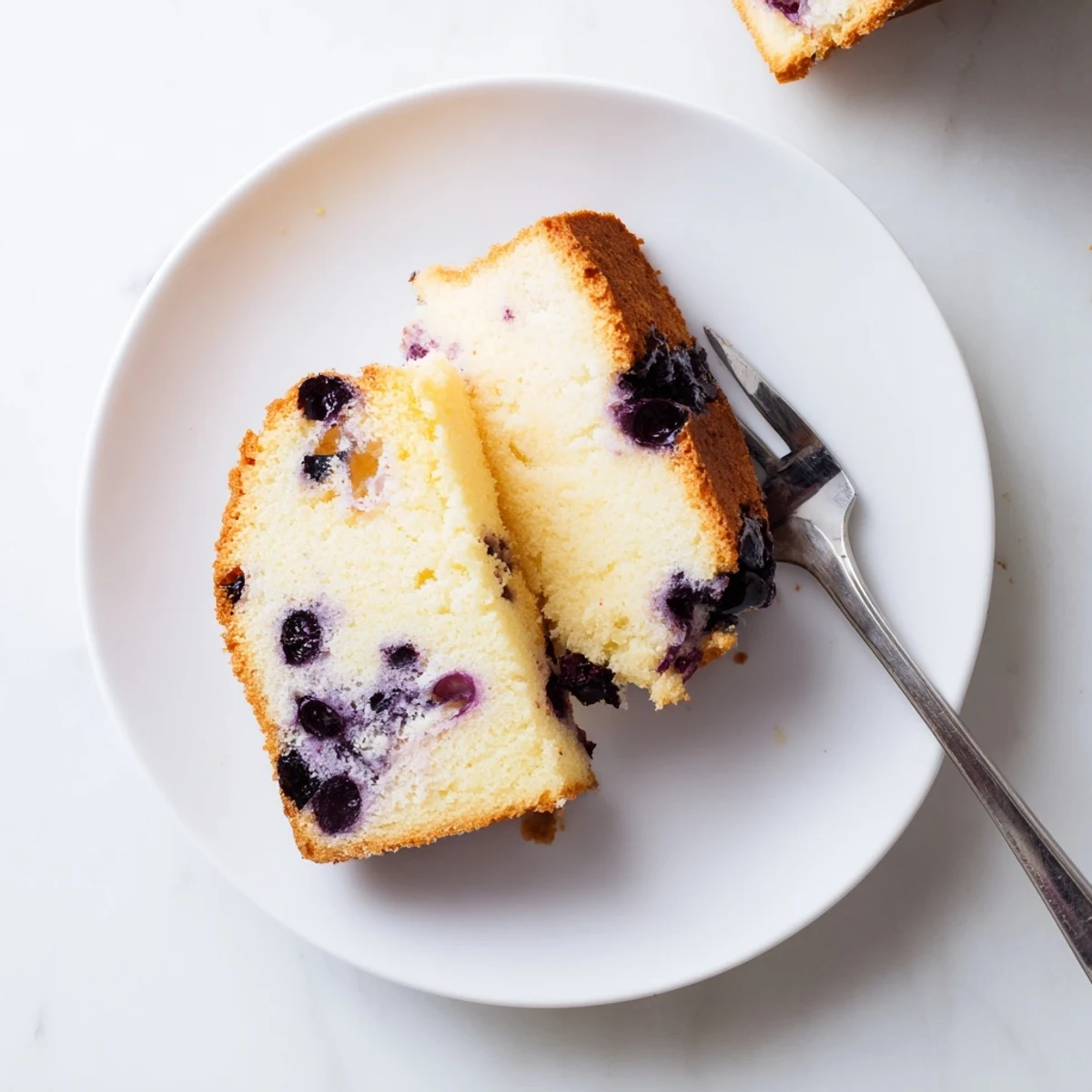 Golden slice of fluffy blueberry chiffon cake topped with fresh berries on a white serving plate