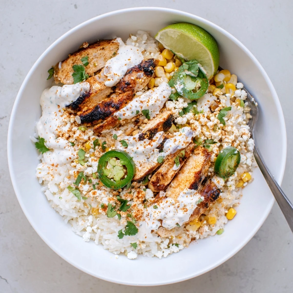 Vibrant street corn chicken rice bowl featuring grilled spiced chicken, charred corn, and zesty lime crema