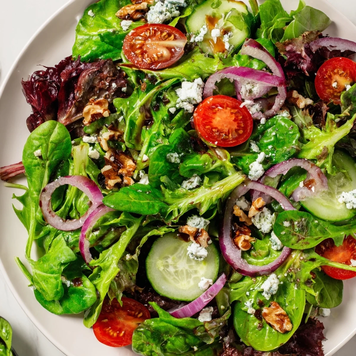 Colorful spring mix salad featuring halved cherry tomatoes, cucumber slices, and glossy balsamic honey dressing coating fresh leaves