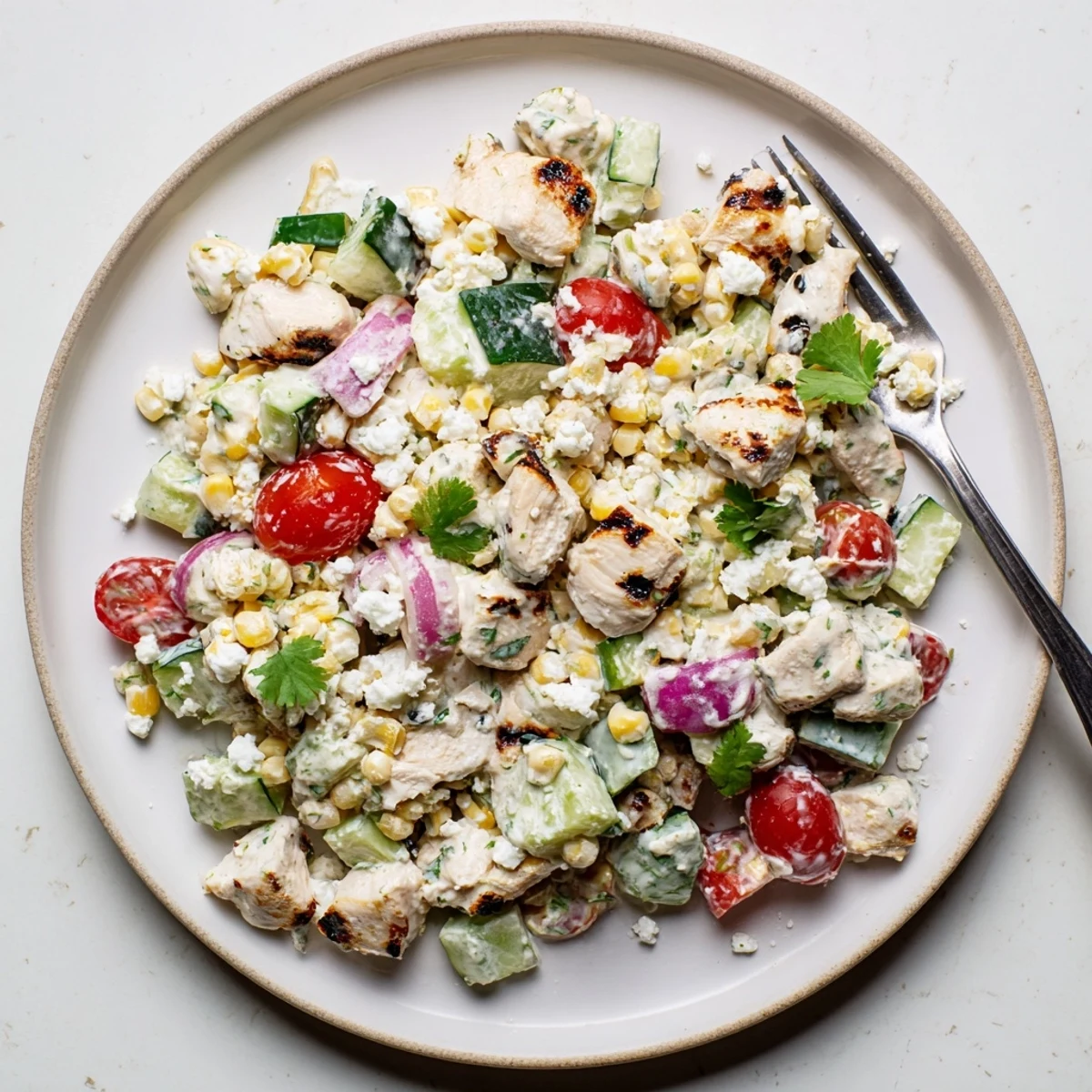 Colorful Tex-Mex chicken salad featuring charred corn cucumber chunks and zesty lime cream sauce garnished with cheese