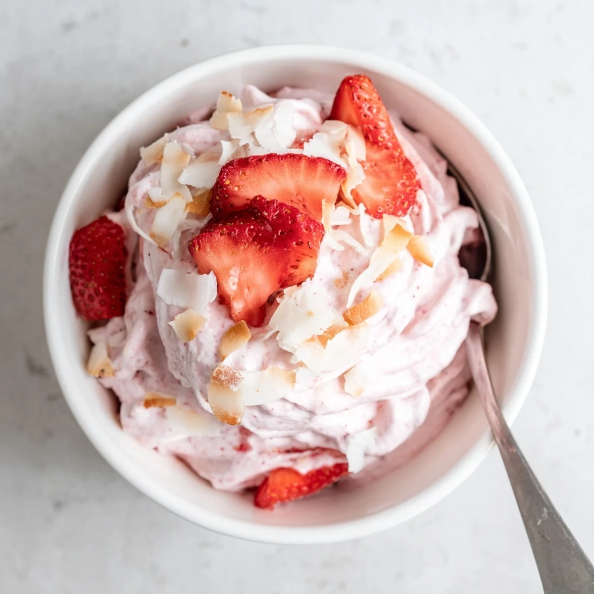 Creamy dairy-free frozen strawberry Dole Whip delight scooped into a waffle cone with toasted coconut