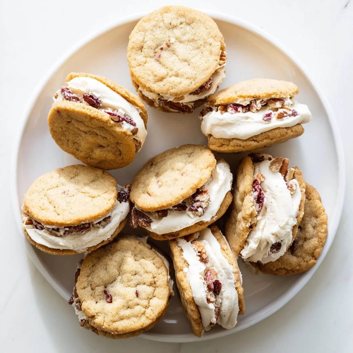 Golden cranberry pecan sandwich cookies stacked with cream cheese filling on white plate