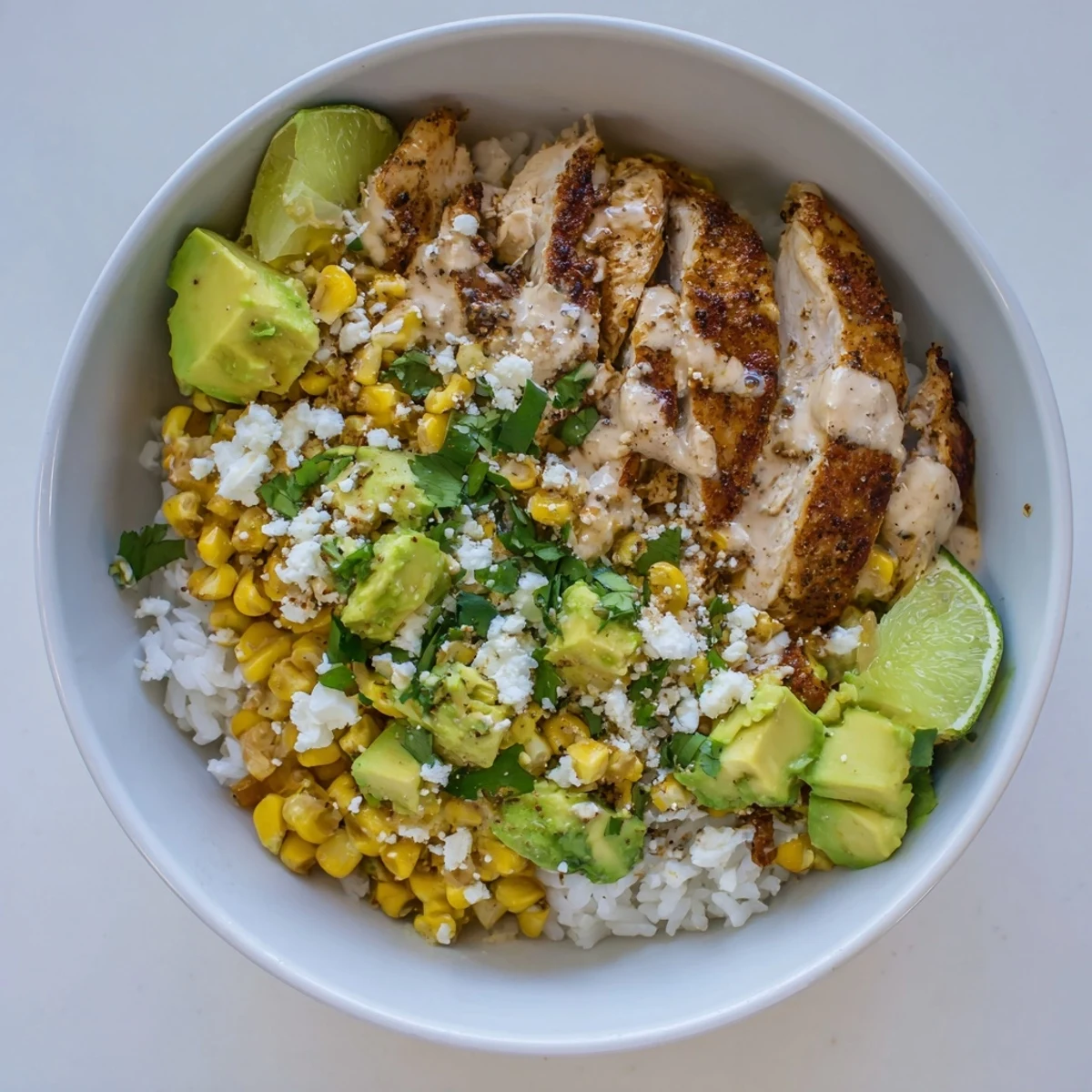 Heaping street corn chicken rice bowl with juicy seasoned meat, tangy mayonnaise-coated corn, crumbled cheese, and bright lime wedges for a satisfying dinner