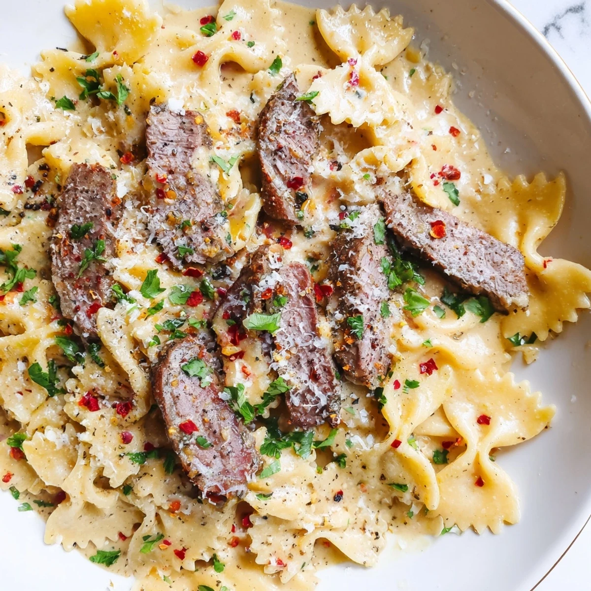 Creamy Cajun Alfredo bowtie pasta topped with seasoned sliced beef and fresh parsley garnish