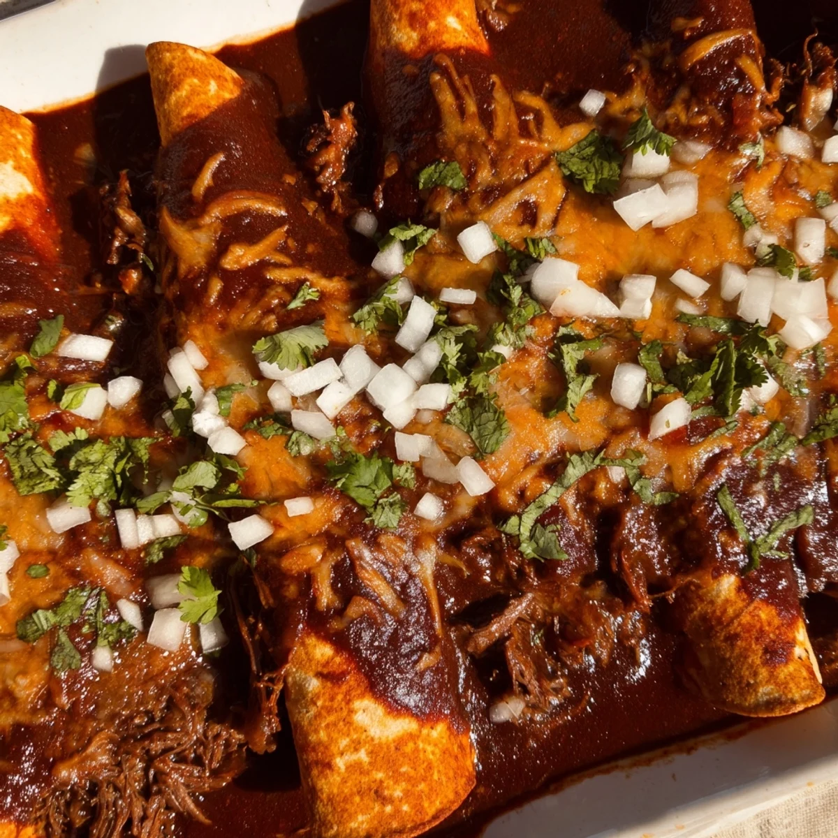 Birria enchiladas plated on a white dish with lime wedges and chopped cilantro garnish
