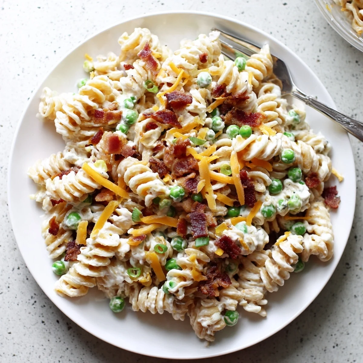 Close-up of savory crack pasta salad with peas, bacon crumbles, and creamy dressing coating rotini noodles