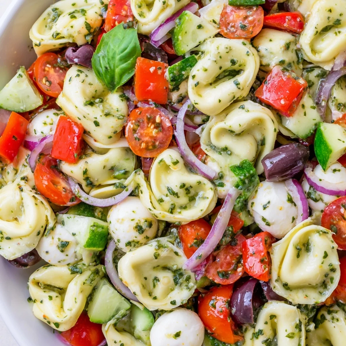 Colorful tortellini salad with ripe cherry tomatoes, crisp cucumber, and zesty herb dressing in a white serving bowl