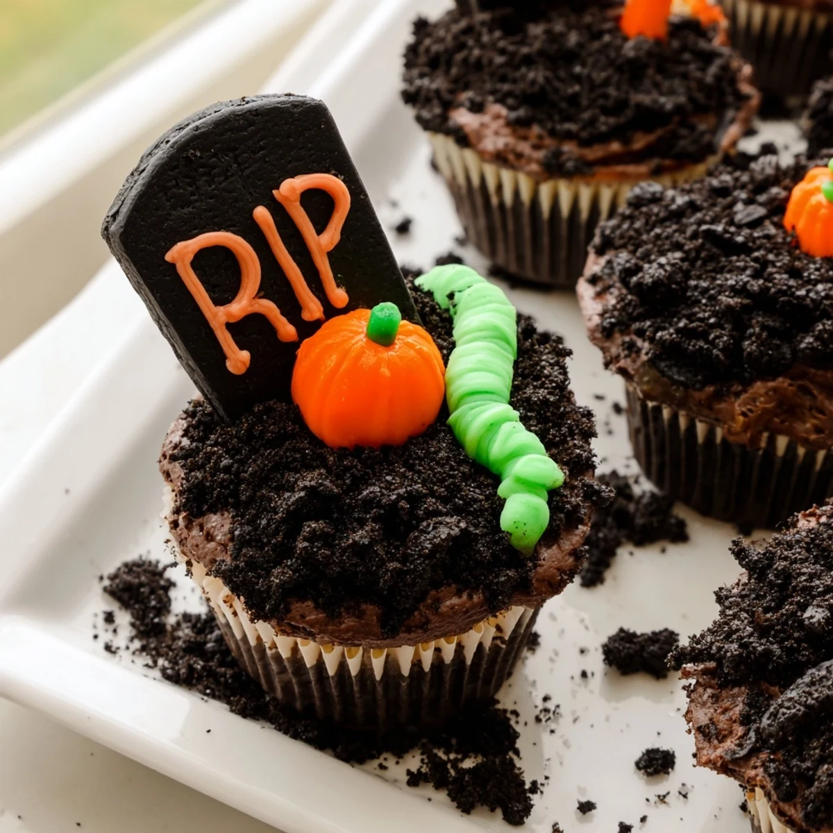 A tray of Pull Apart Graveyard Cupcakes featuring edible tombstones and candy pumpkin decorations on dark chocolate frosting