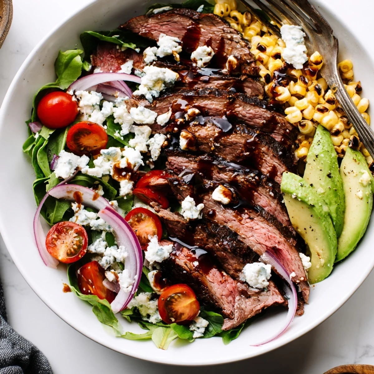 A plated balsamic steak Gorgonzola salad drizzled with vinaigrette alongside sweet grilled corn