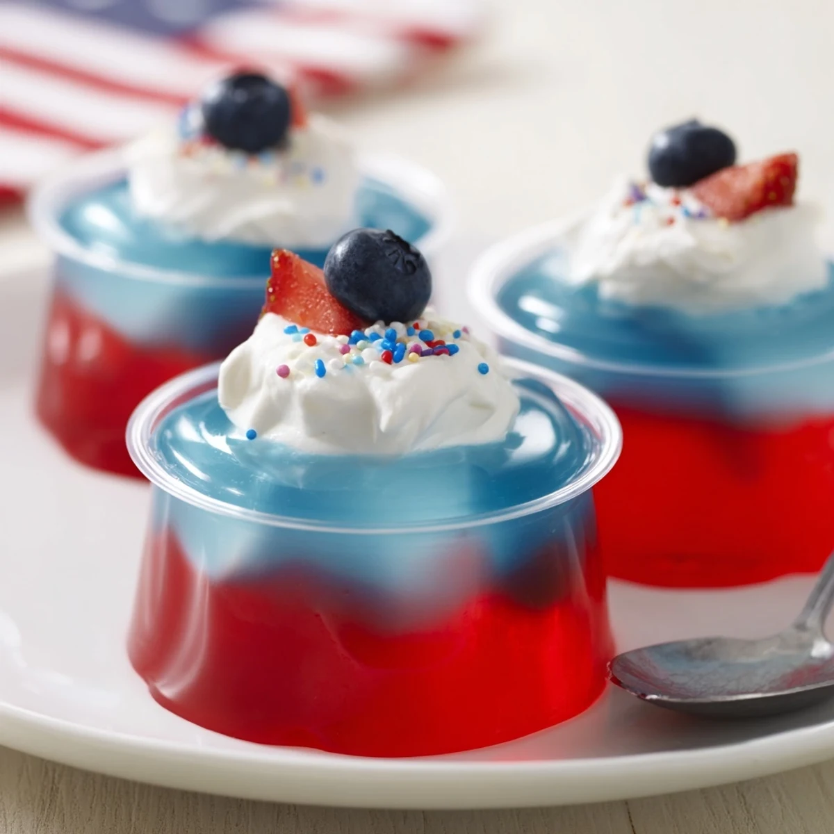 Chilled Red White And Blue Jello Cups topped with whipped cream and berries