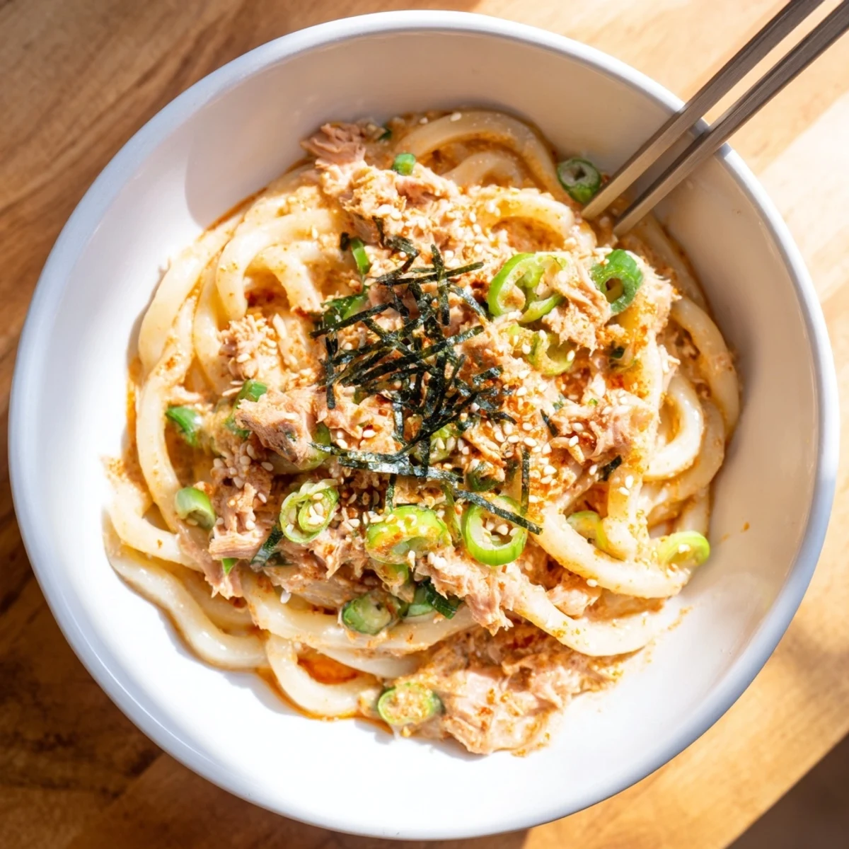 Bowl of Japanese fusion spicy tuna udon garnished with sesame seeds and nori strips